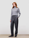 Woman wearing a gray turtleneck and dark gray pants on a plain background