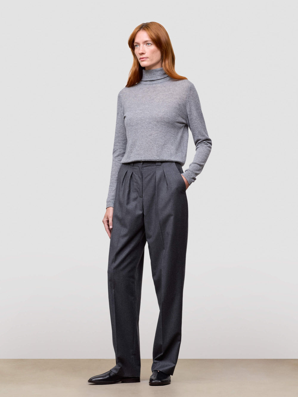 Woman wearing a gray turtleneck and dark gray pants on a plain background