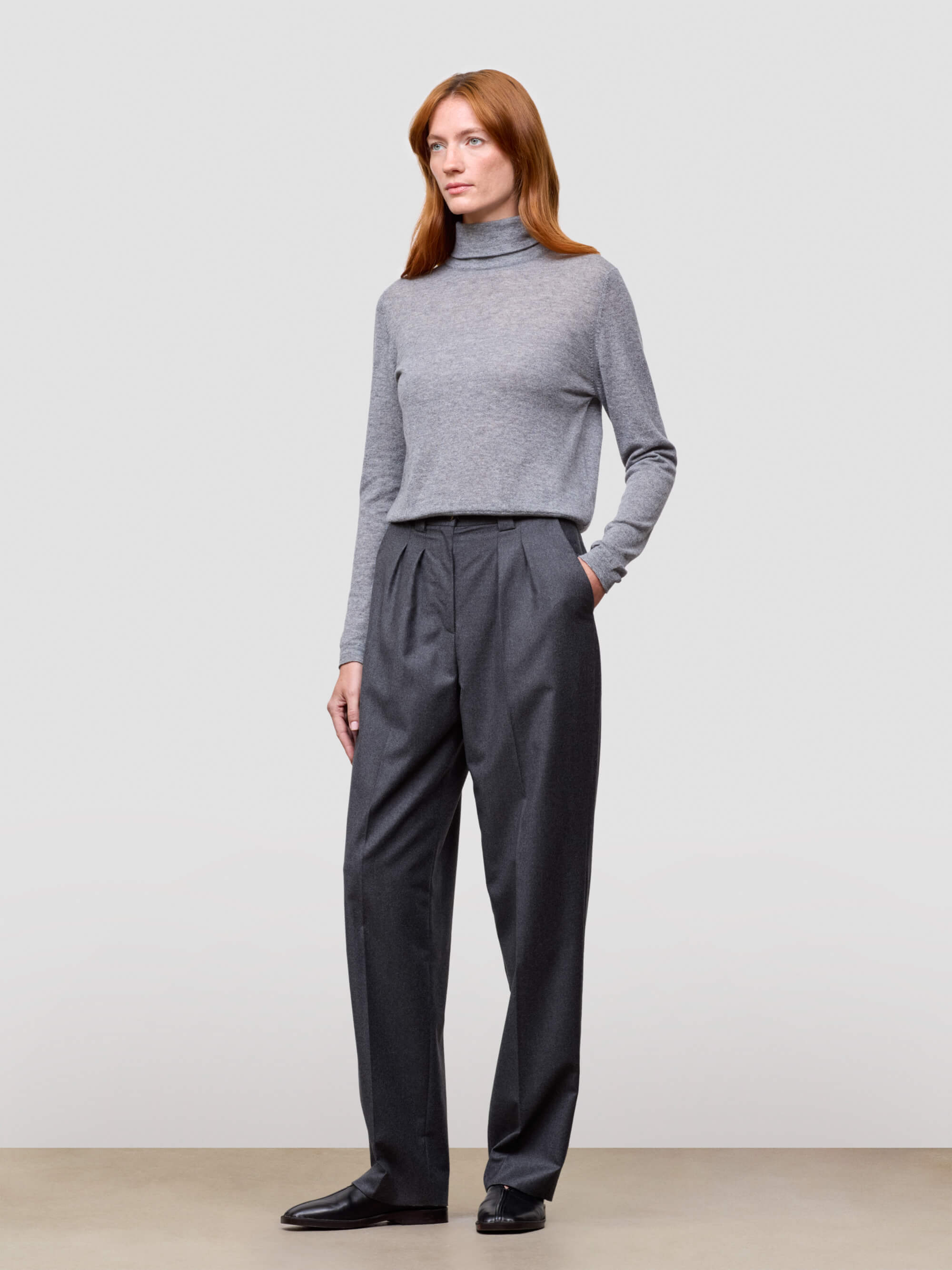 Woman wearing a gray turtleneck and dark gray pants on a plain background