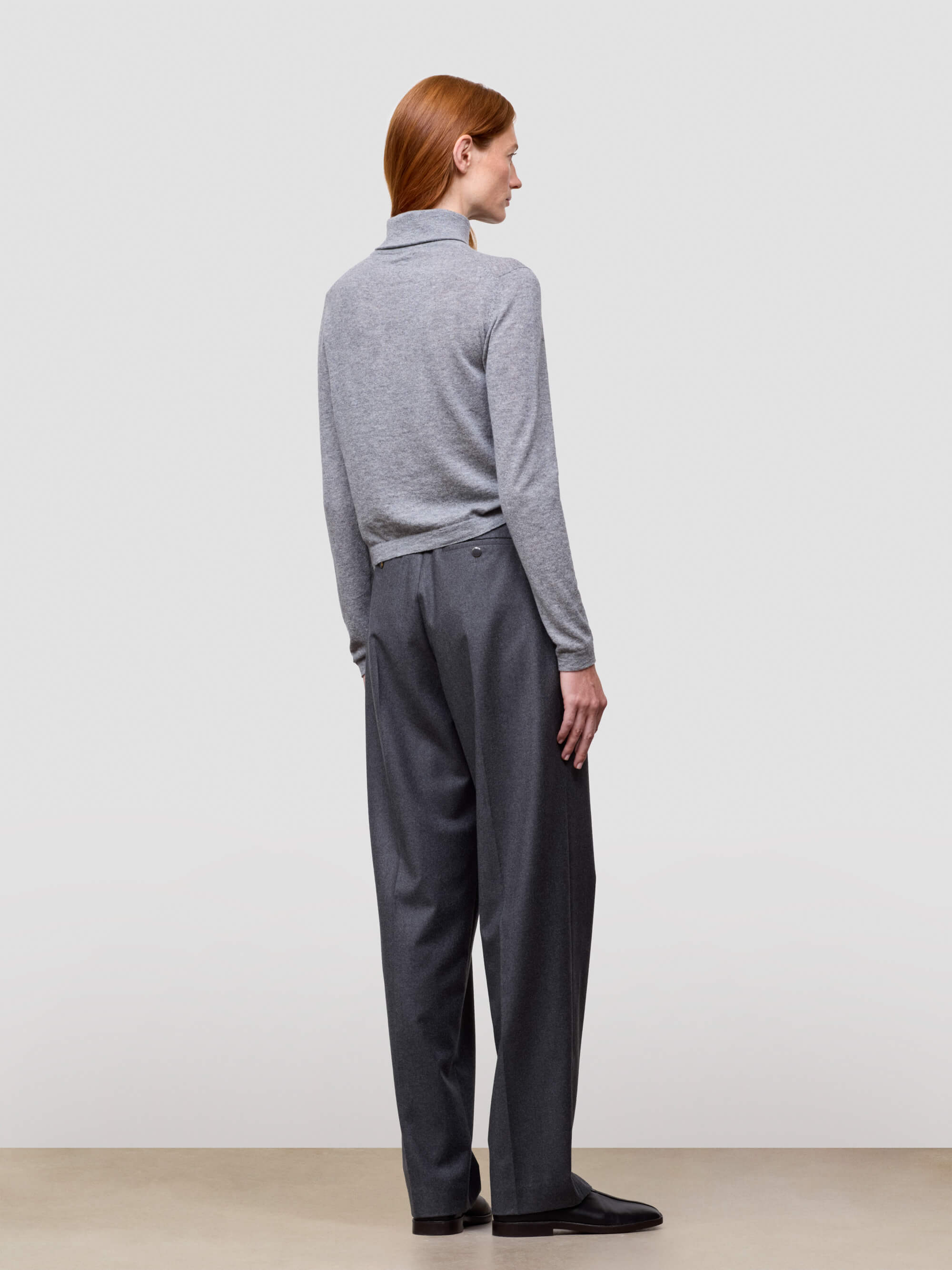 woman wearing a gray sweater and dark pants against a white background