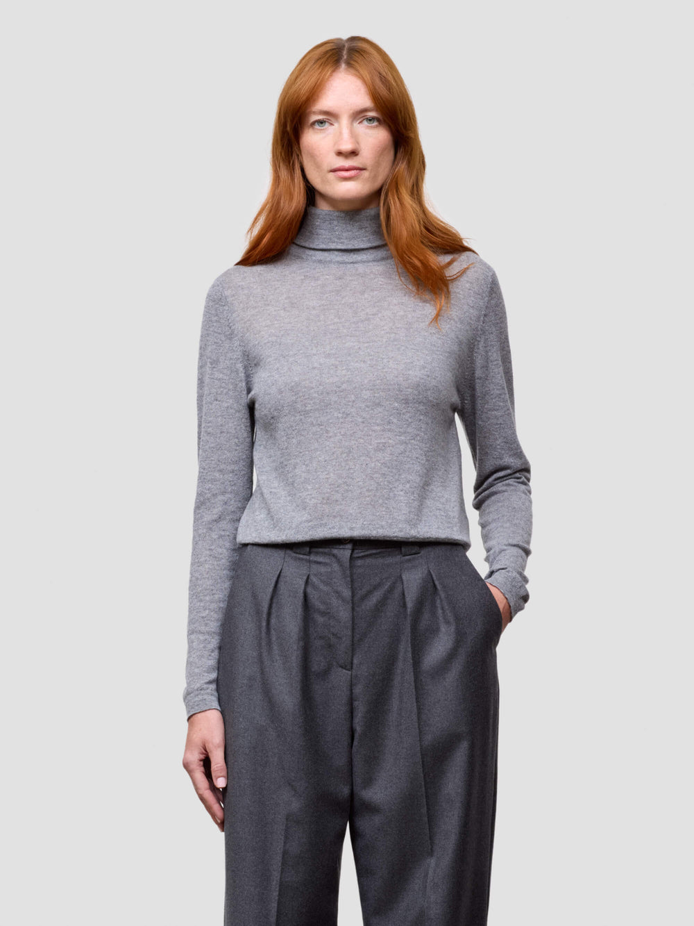 woman wearing a gray turtleneck sweater and dark gray pants on a light gray background
