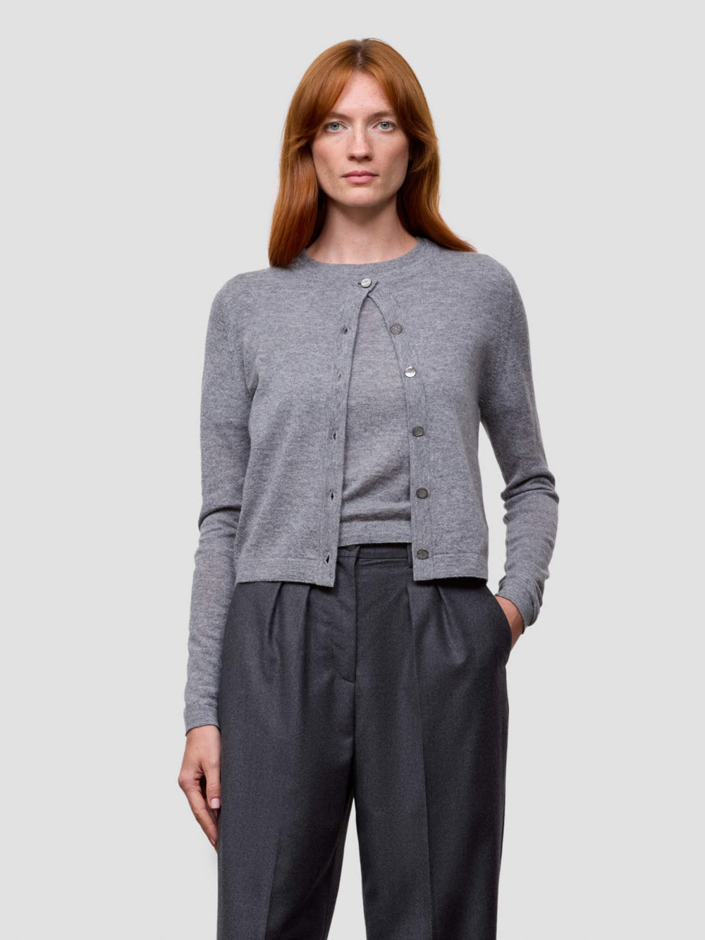 Woman wearing a gray cashmere cardigan and dark pants on a light gray background