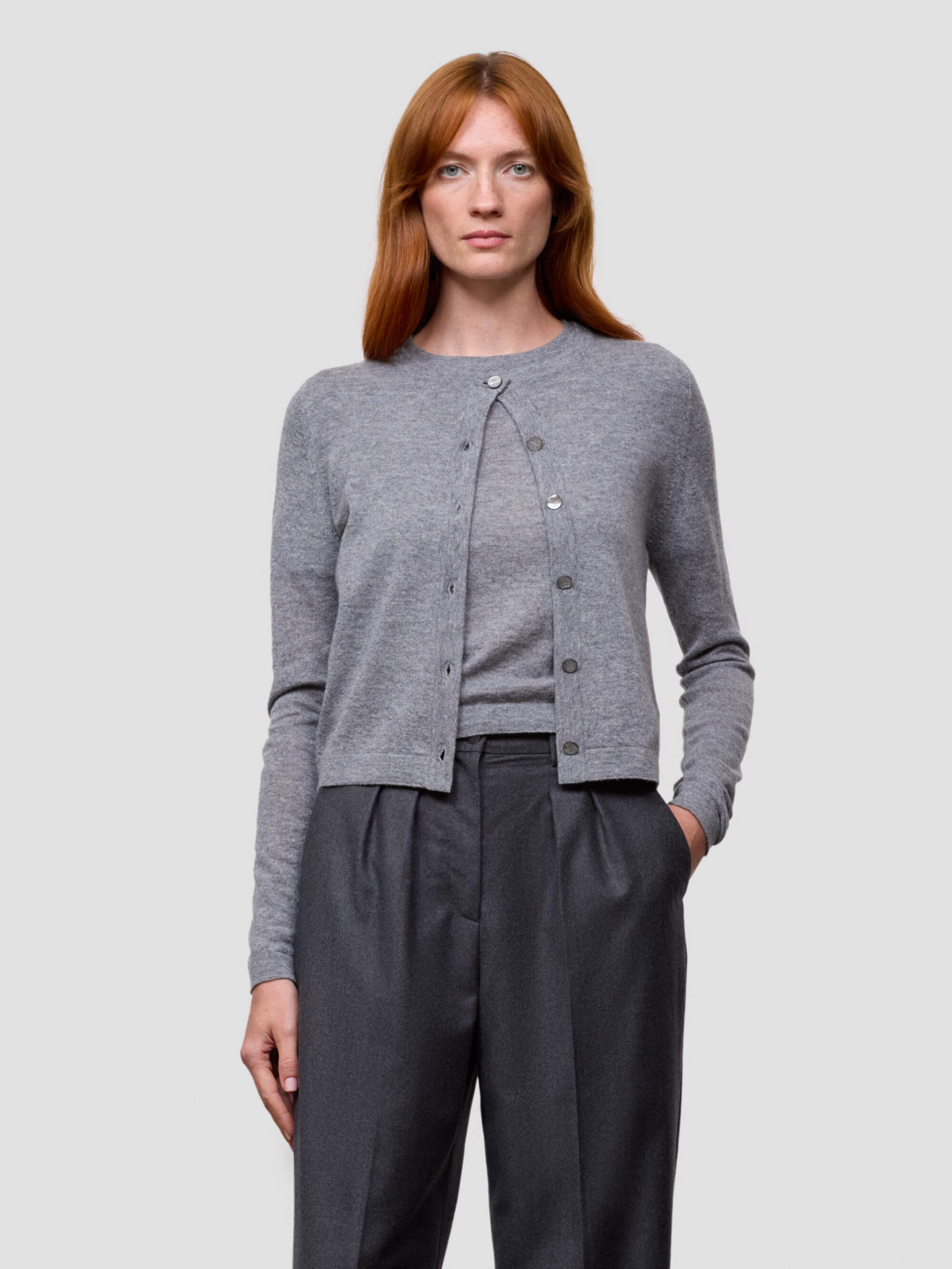 Woman wearing a gray cashmere cardigan and dark pants on a light gray background