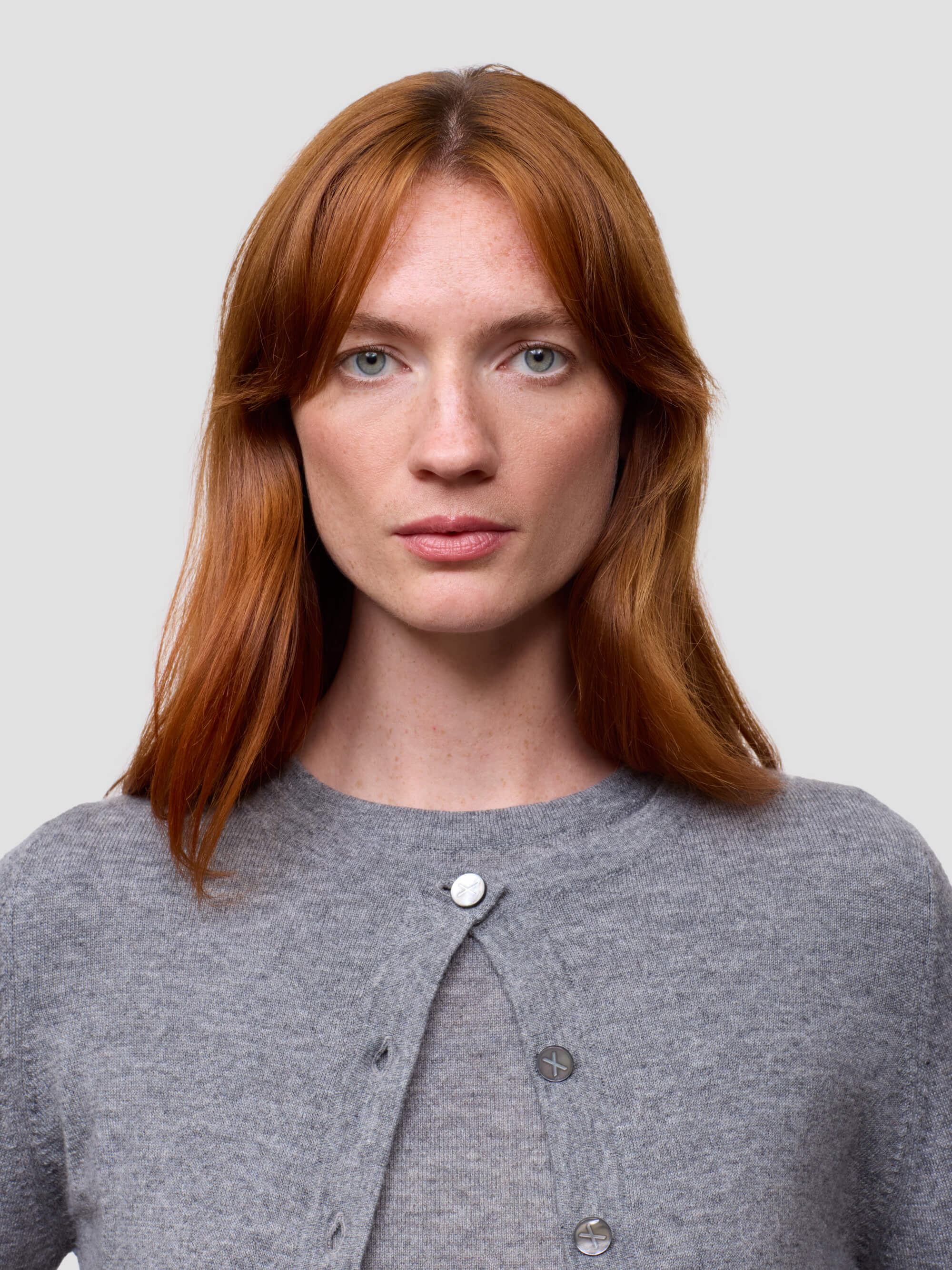 Woman with red hair wearing a gray cardigan against a plain background