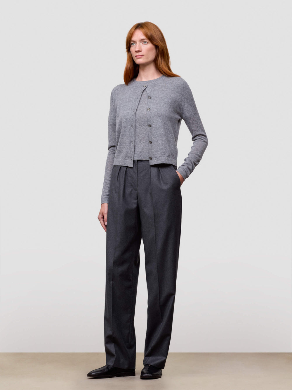 woman wearing grey cashmere cardigan and grey trousers on a white background