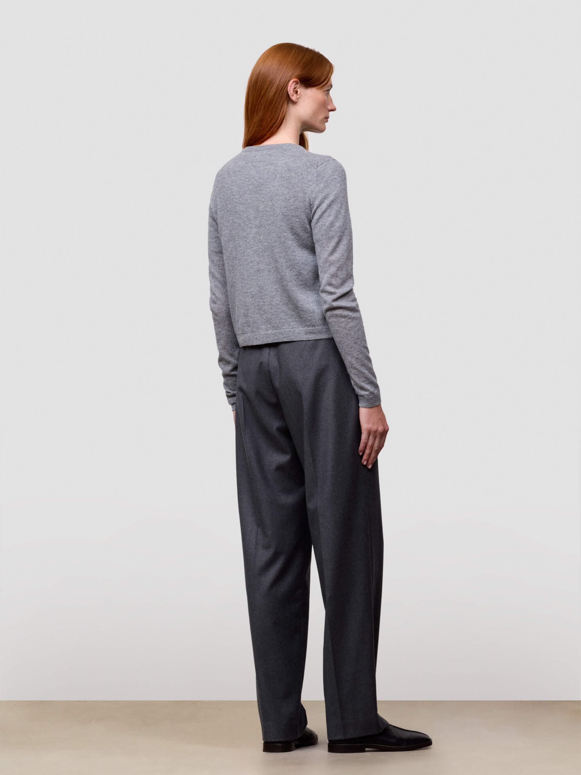 Person wearing a gray cardigan and dark pants against a white background