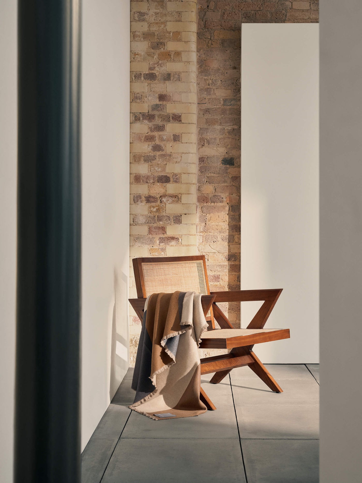 Wooden chair with a cashmere blanket draped over it against a brick wall.