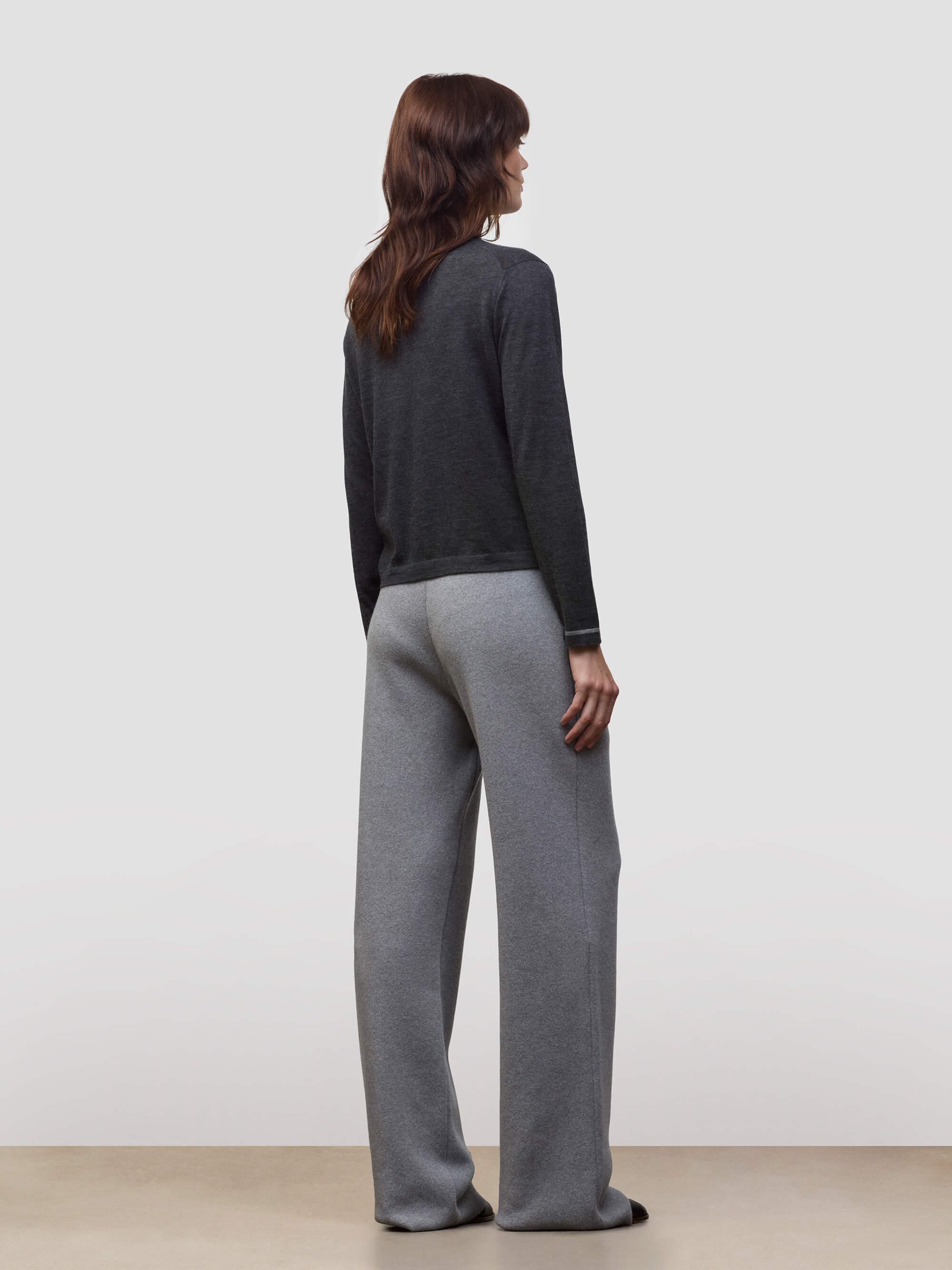Woman wearing a dark gray cashmere sweater and light gray cashmere pants on a white background