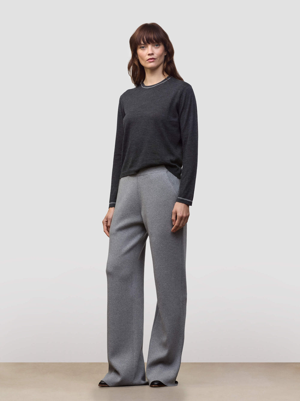 Woman wearing a dark gray cashmere sweater and light gray cashmere pants on a white background