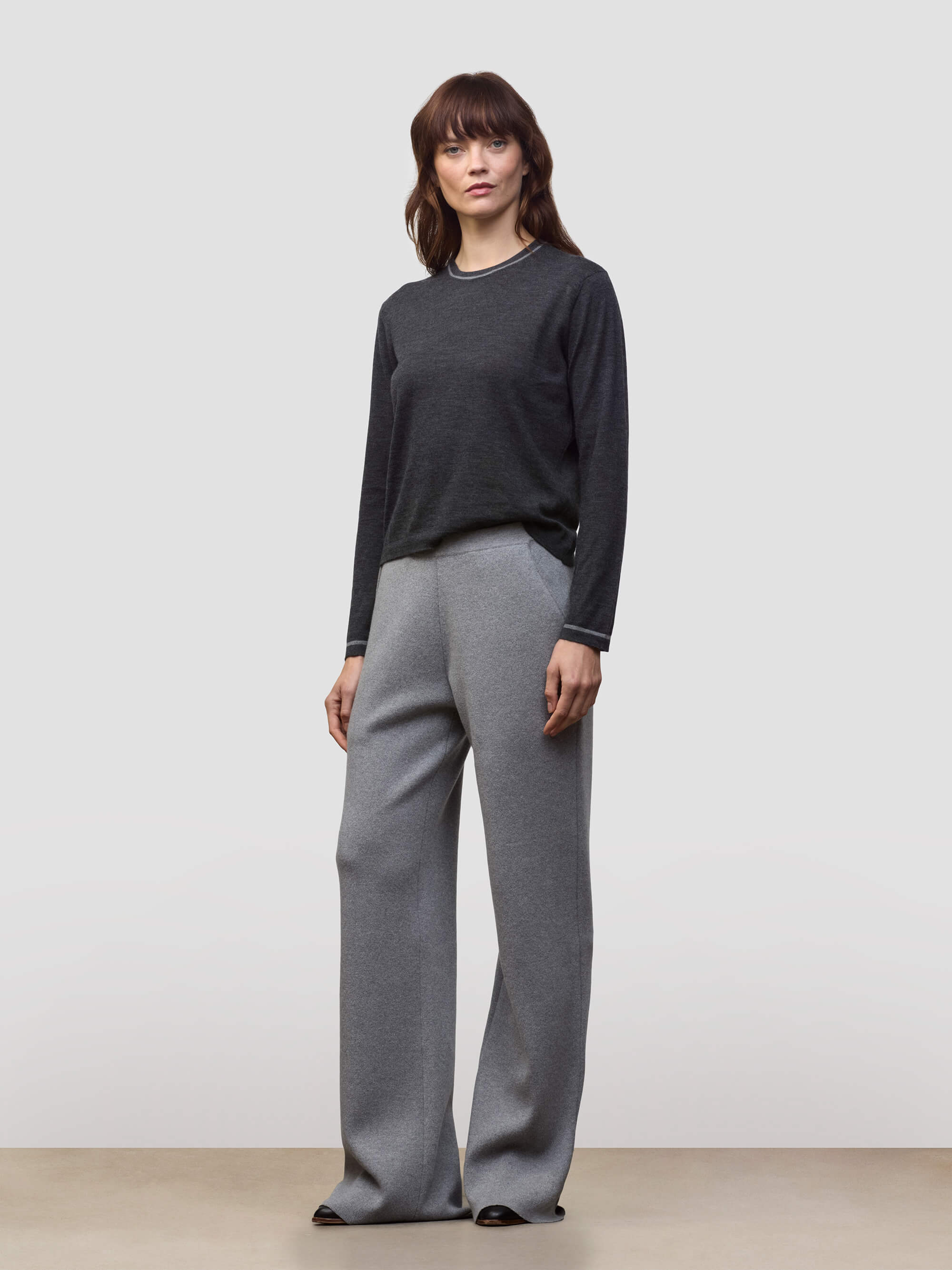 Woman wearing a dark gray cashmere sweater and light gray cashmere pants on a white background