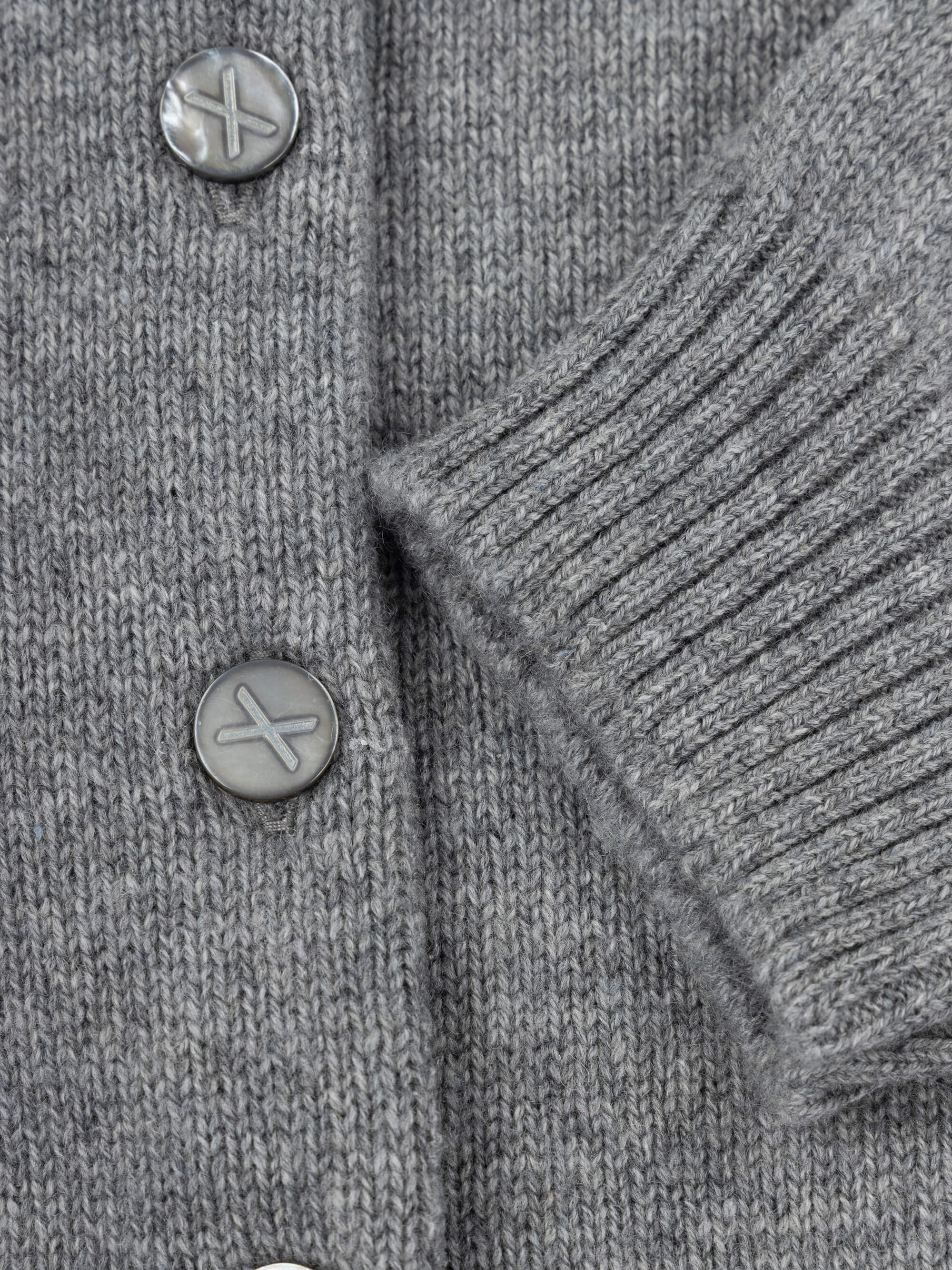 Close-up of a gray knitted cardigan with buttons on a plain background