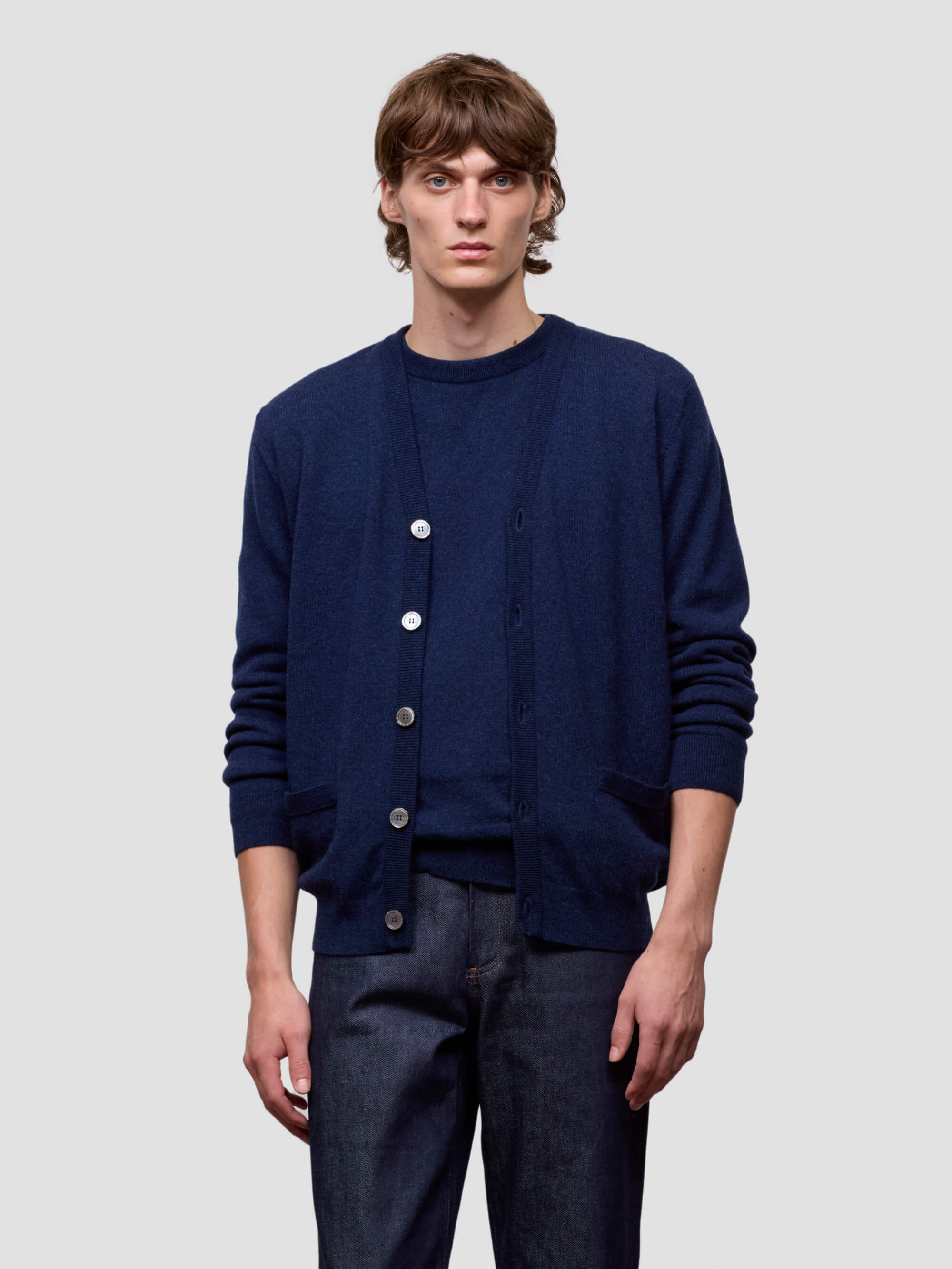 Man wearing a navy blue cardigan over a dark shirt with matching pants on a light gray background