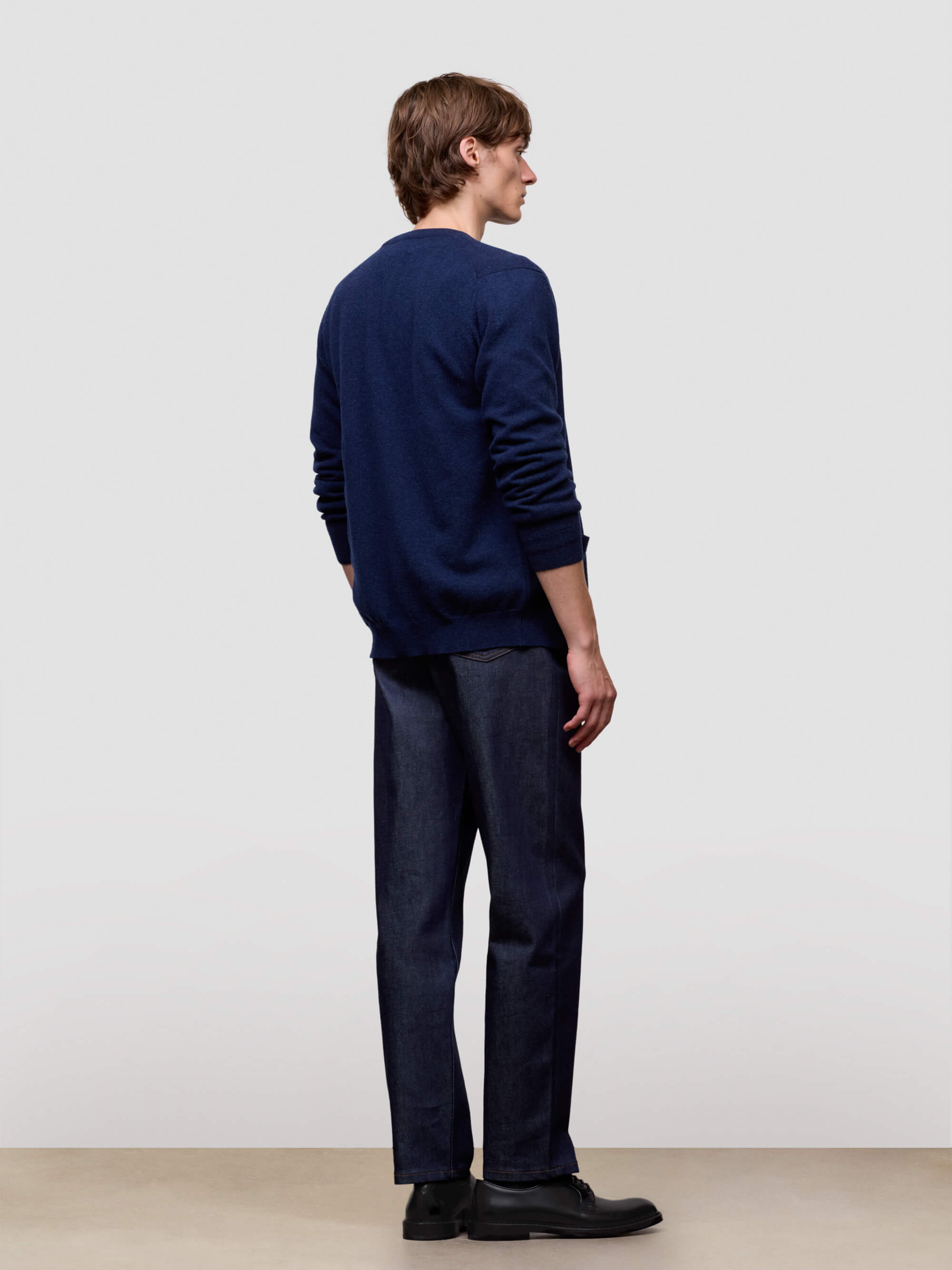 Man wearing a navy sweater and dark pants against a plain background