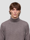 Man wearing a brown turtleneck sweater against a plain background
