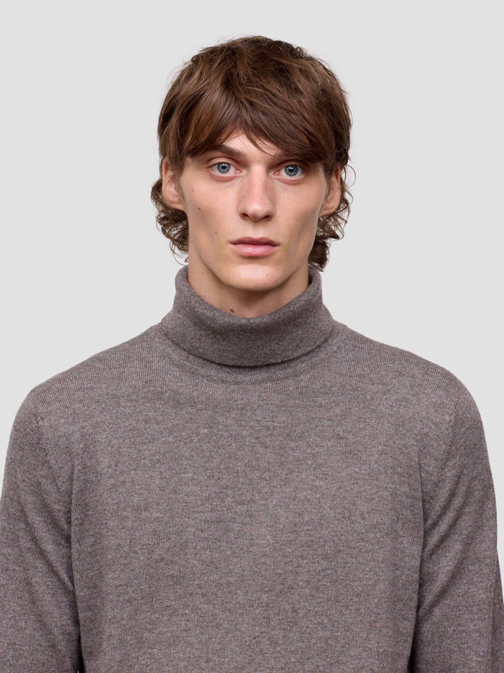 Man wearing a brown turtleneck sweater against a plain background