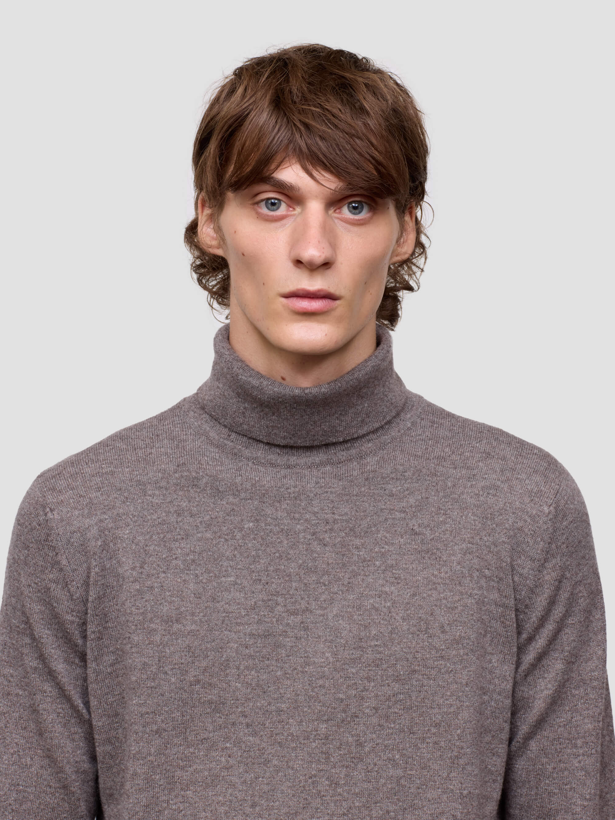 Man wearing a brown turtleneck sweater against a plain background