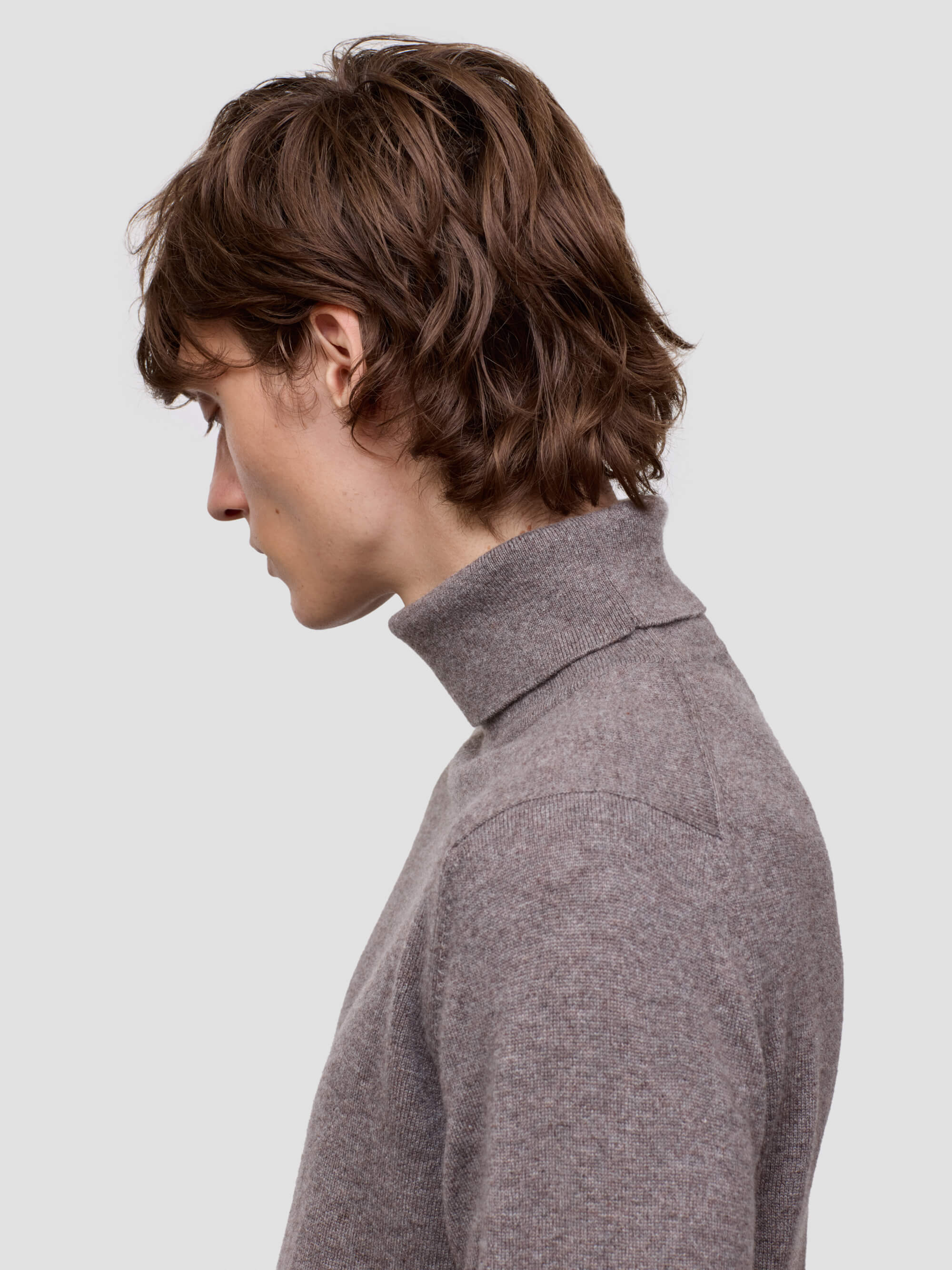 Person wearing a brown turtleneck sweater on a light gray background