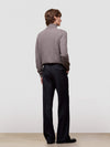Person wearing a brown sweater and black pants against a white background