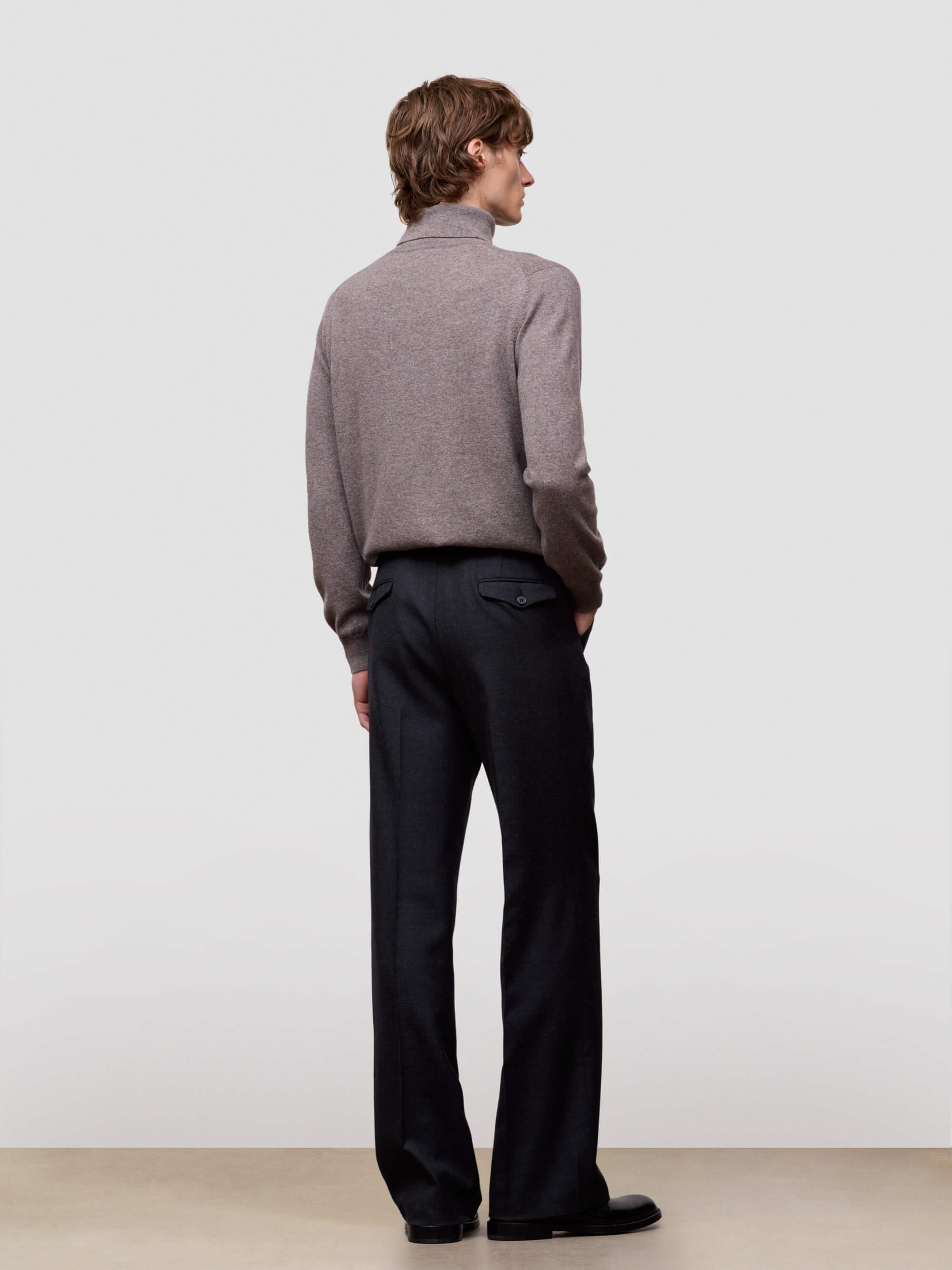 Person wearing a brown sweater and black pants against a white background