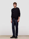 Man wearing a black cardigan and dark pants against a plain background