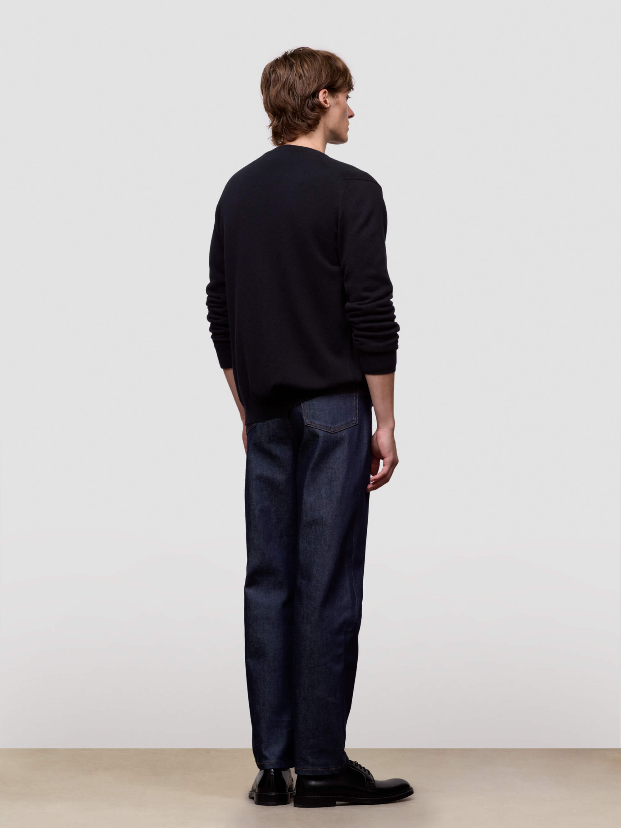 Person wearing a black sweater and dark pants against a white background