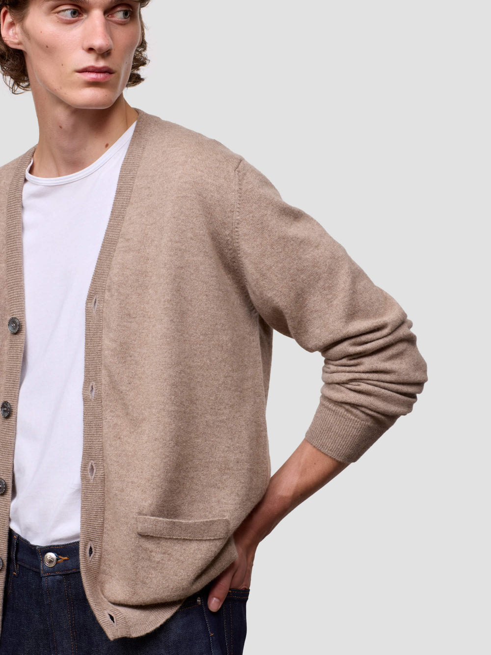 Man wearing a beige cardigan over a white shirt on a plain background