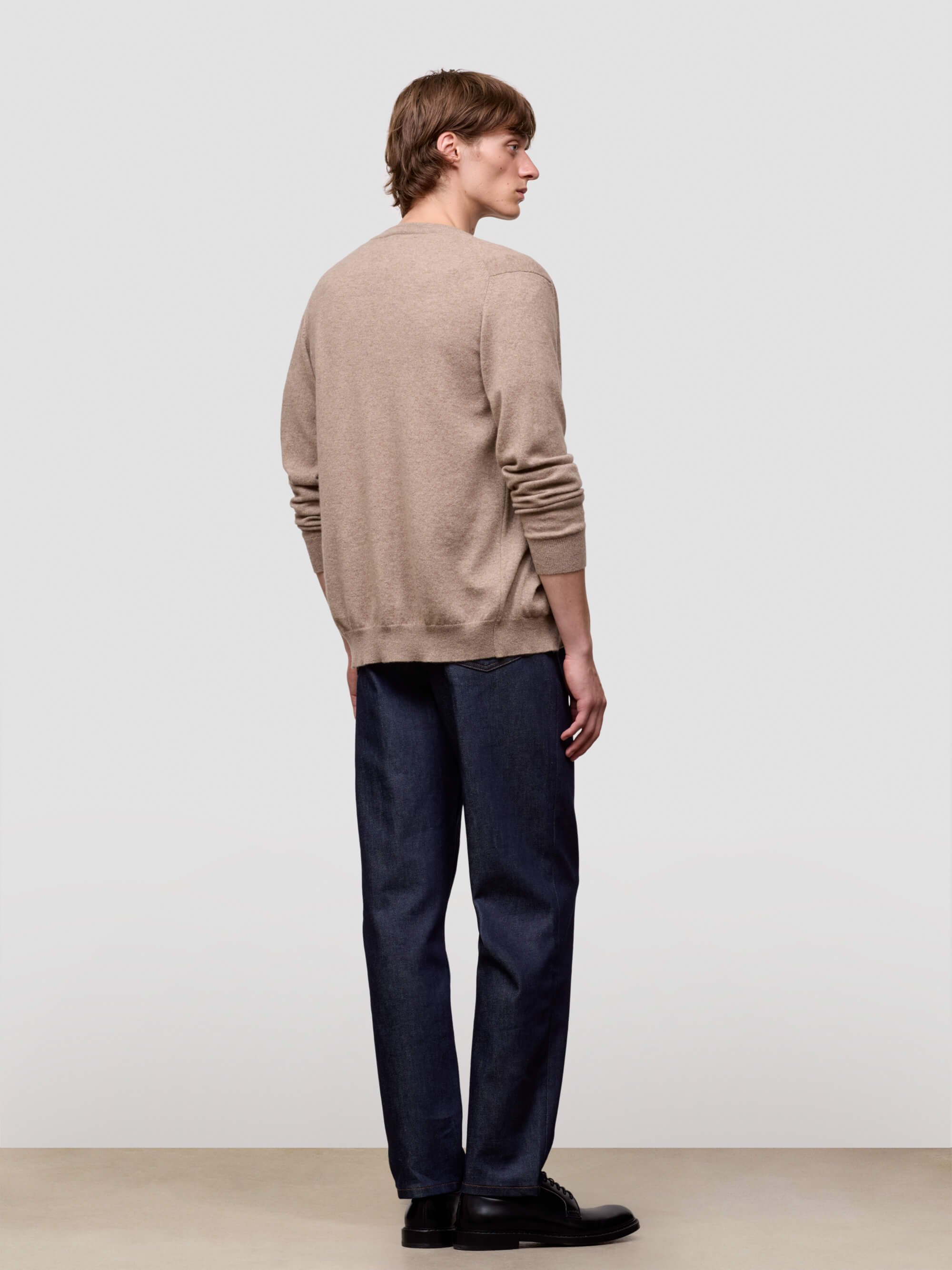 Person wearing a beige sweater and dark pants on a plain background