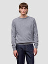Man wearing a gray cashmere sweater and dark pants on a light gray background