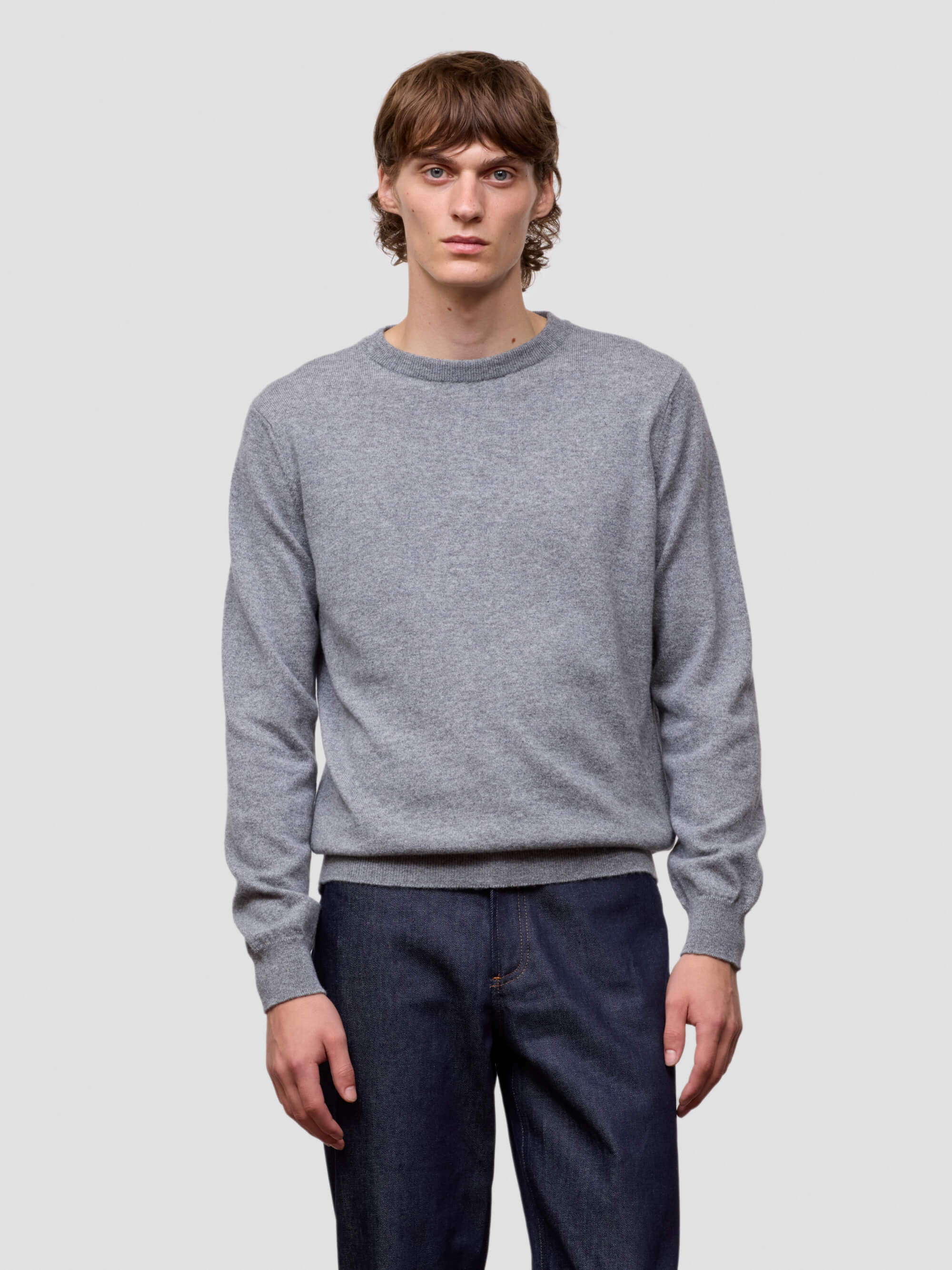 Man wearing a gray cashmere sweater and dark pants on a light gray background