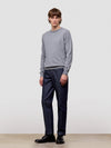 Man wearing a gray cashmere sweater and dark pants against a plain background