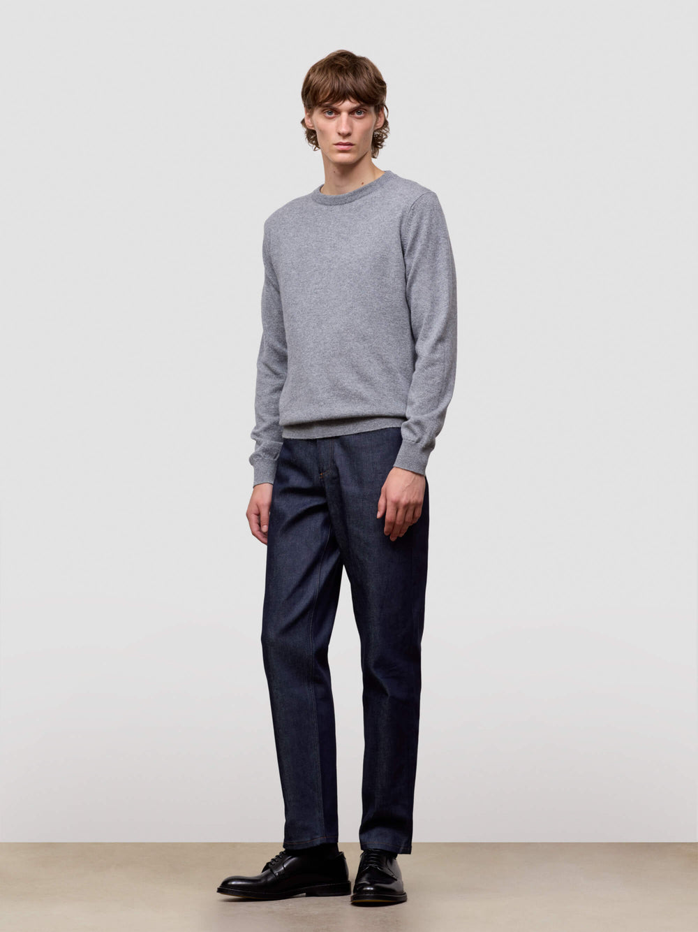 Man wearing a gray cashmere sweater and dark pants against a plain background