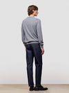 Person wearing a gray sweater and dark jeans standing against a plain white background