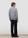 Man wearing a gray half zip sweater and black pants against a white background