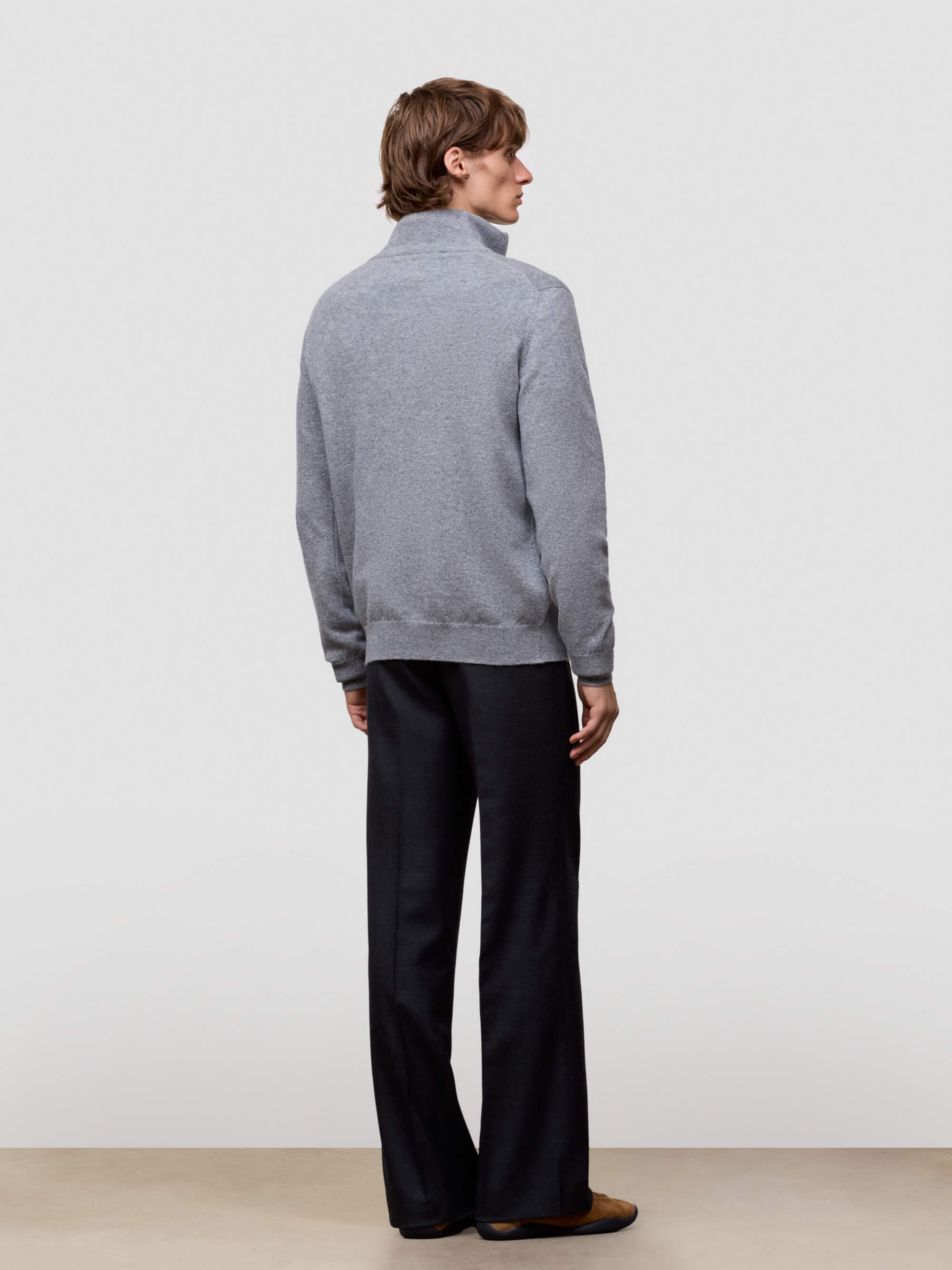 Man wearing a gray half zip sweater and black pants against a white background