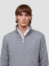 Man wearing a gray half zip cashmere sweater over a white shirt against a plain background
