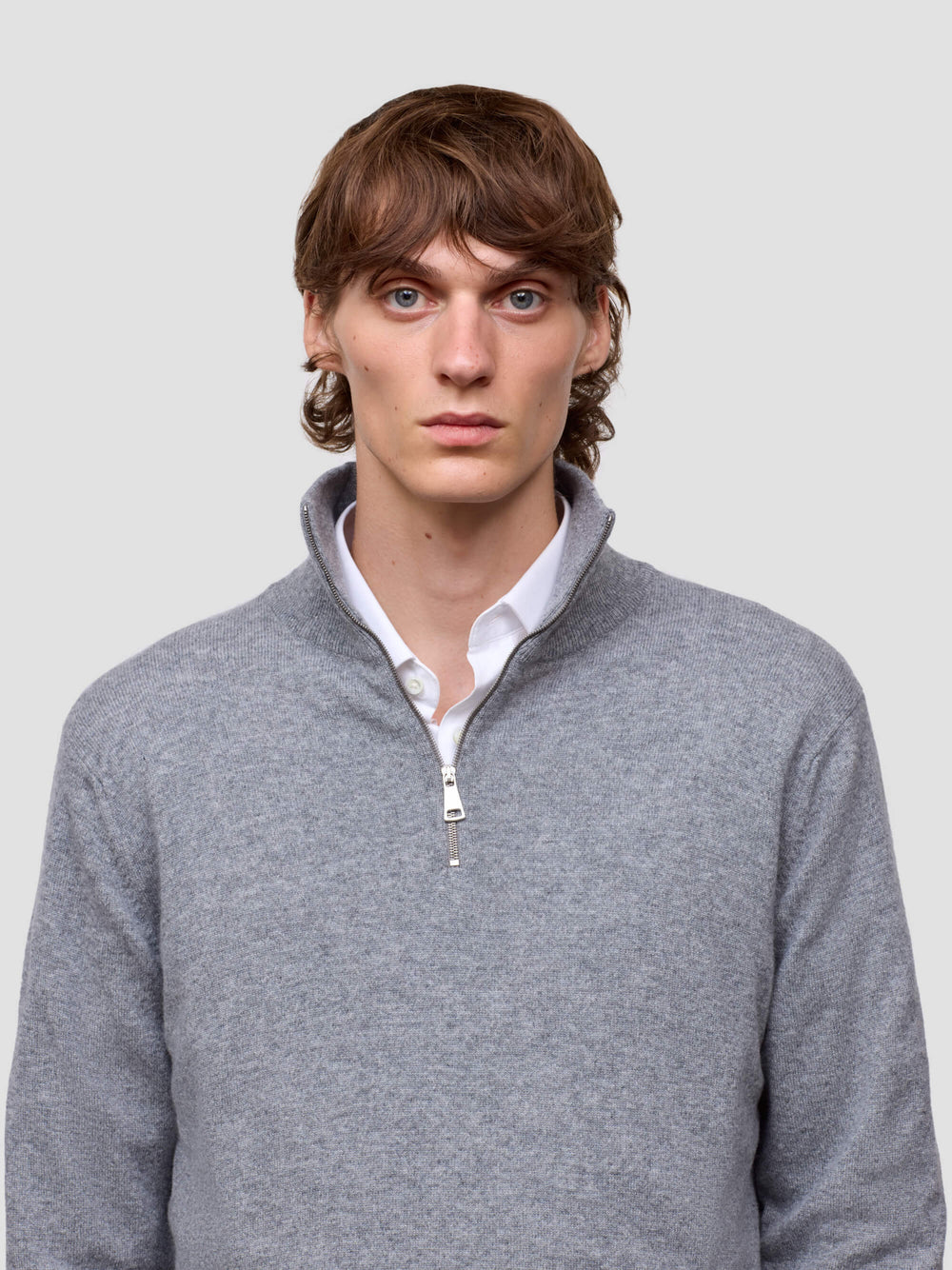 Man wearing a gray half zip cashmere sweater over a white shirt against a plain background
