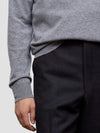 Person wearing a gray sweater and black pants on a light gray background