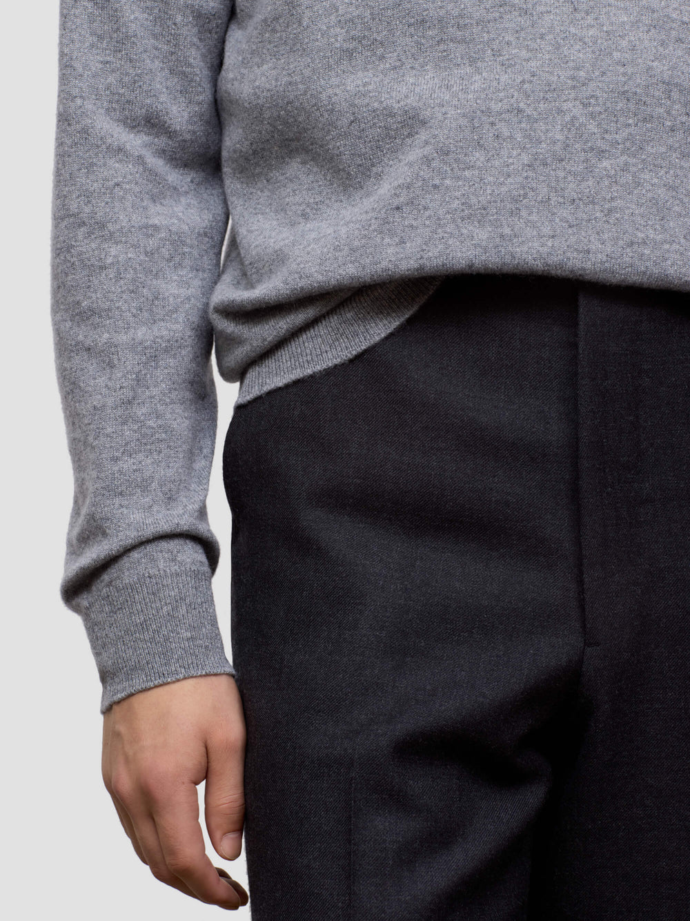 Person wearing a gray sweater and black pants on a light gray background
