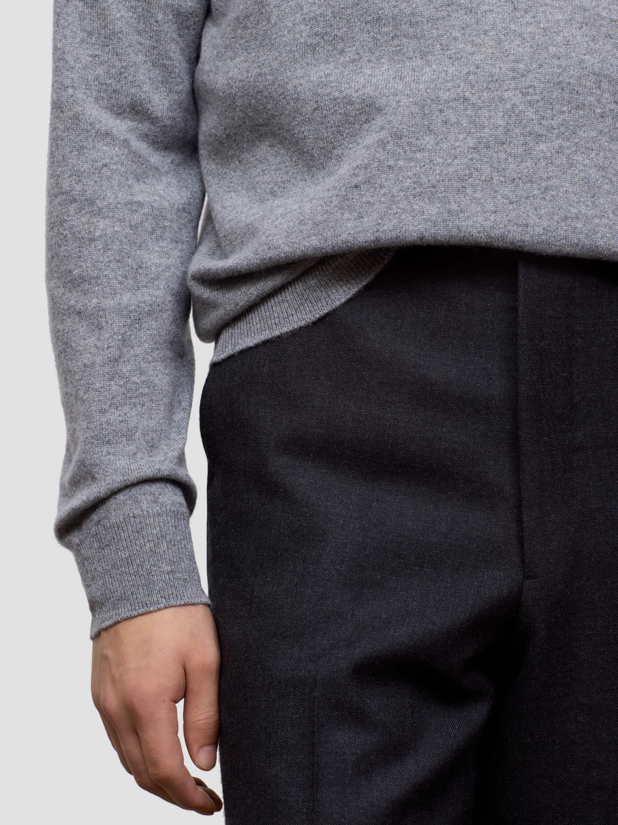Person wearing a gray sweater and black pants on a light gray background