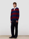 Man wearing a red and blue striped sweater with a white shirt underneath, standing against a plain background.