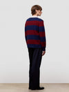 Person wearing a red and blue striped cashmere sweater with dark pants on a plain background