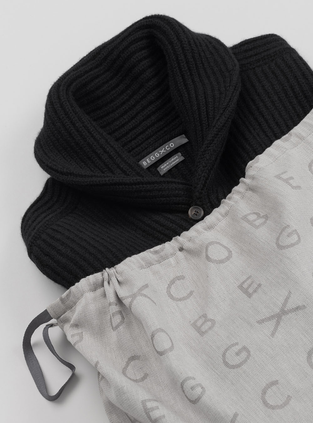 Black ribbed cashmere cardigan, folded and tucked into a Begg x Co garment bag for excellent cashmere care in storage - Begg x Co