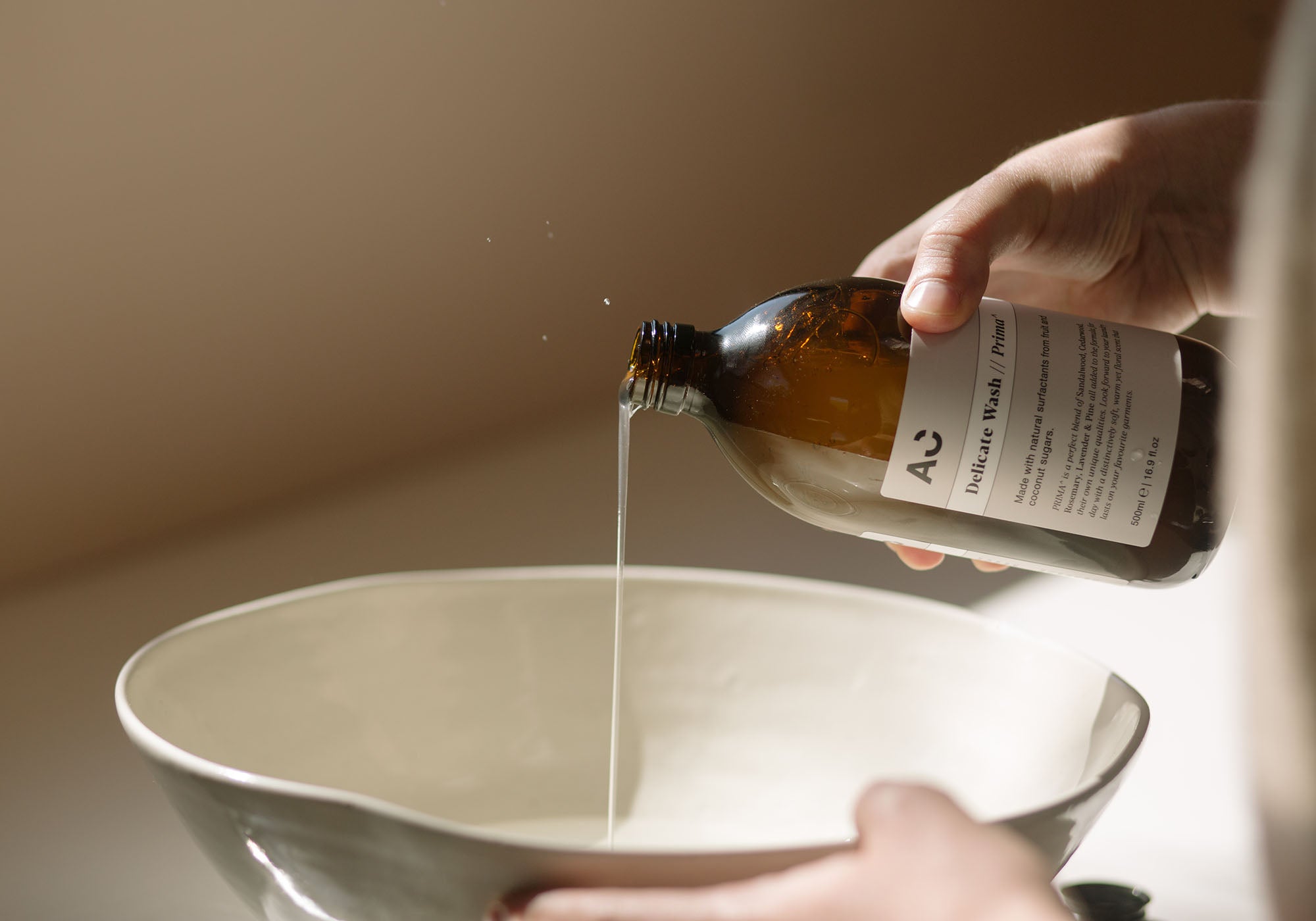 Someone pouring cashmere shampoo from a brown bottle into a ceramic bowl, demonstrating how to wash cashmere- Begg x Co.