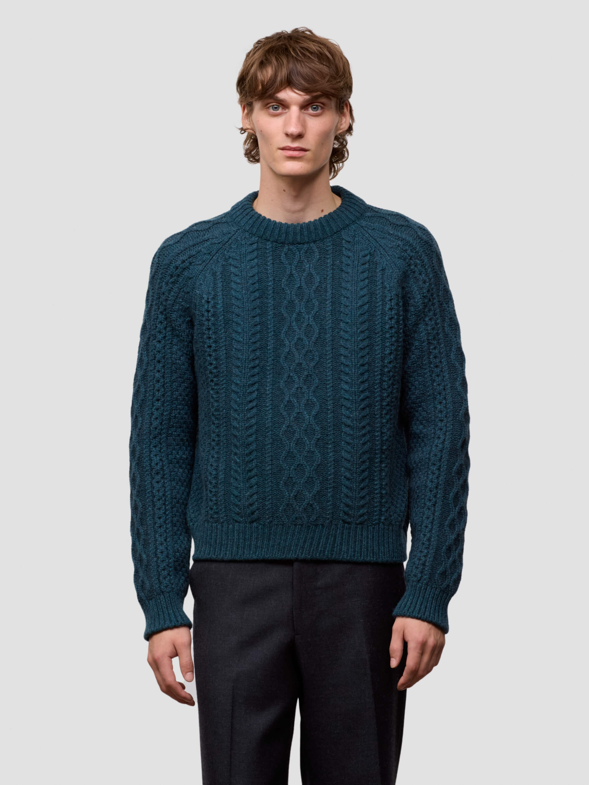 Man wearing a teal knitted sweater against a plain background