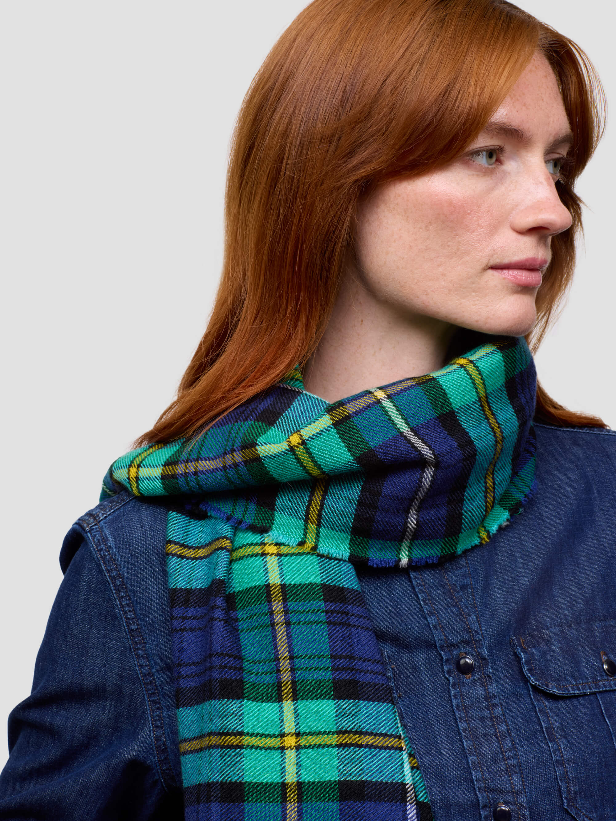 Woman wearing a green and blue plaid scarf against a plain background