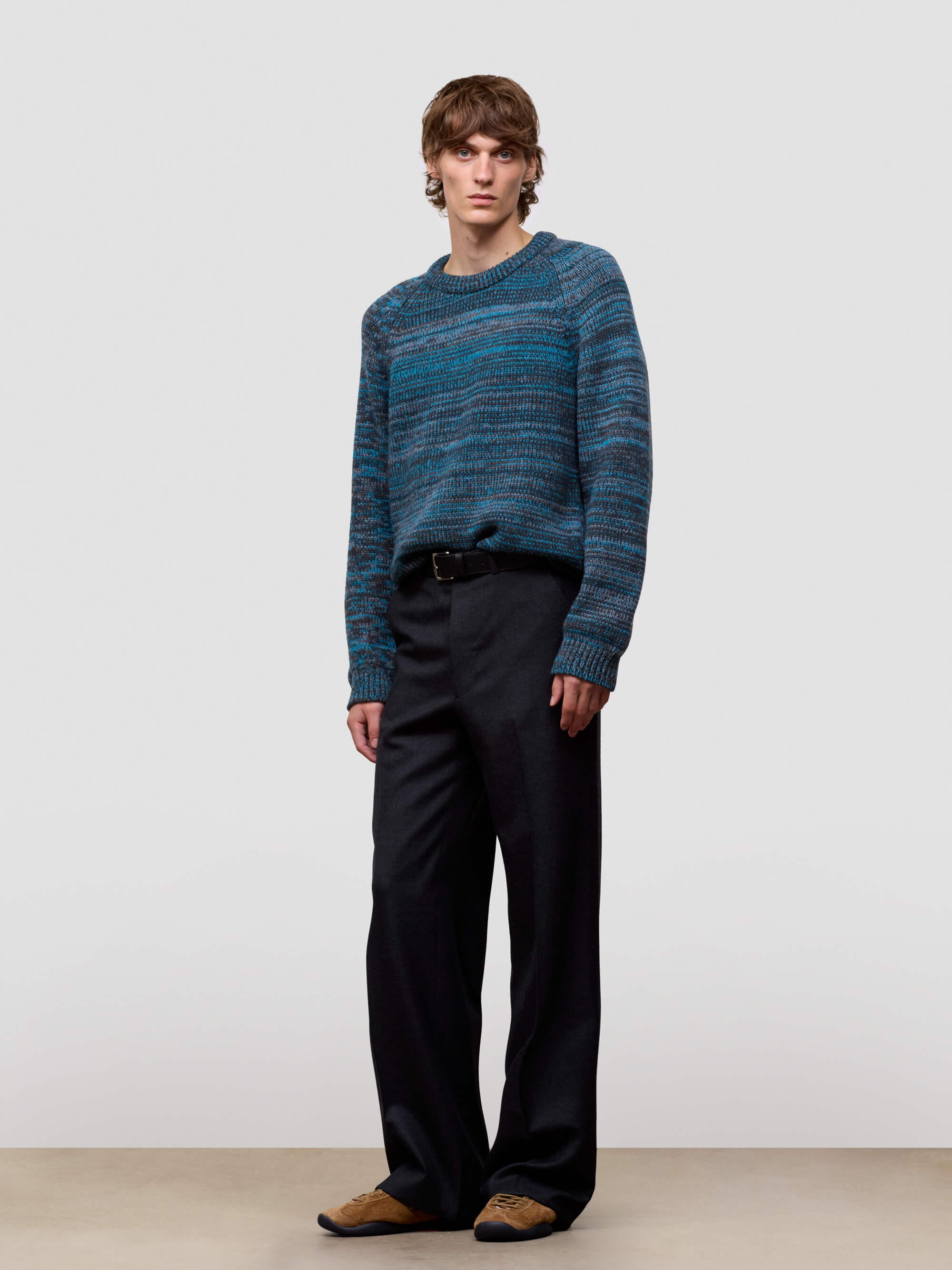 Man wearing a blue patterned cashmere sweater and black pants on a white background