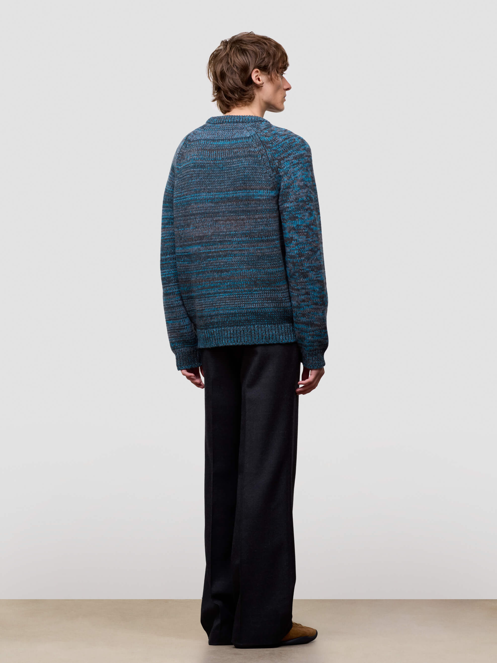 man wearing a blue cashmere knitted sweater and black pants against a white background