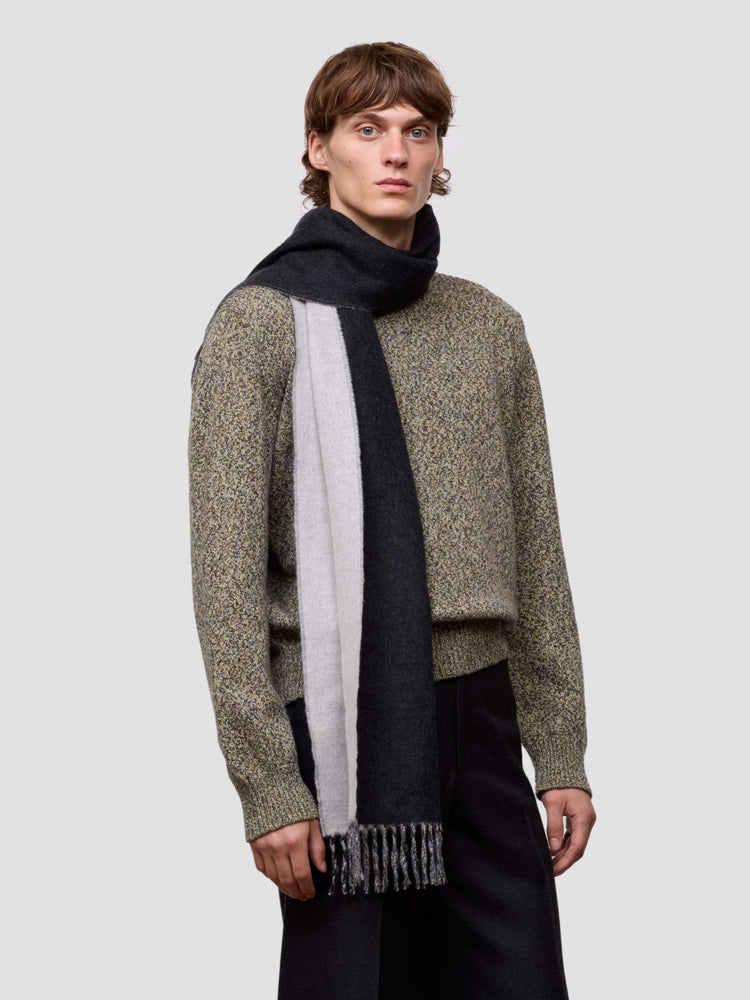 Man wearing a patterned sweater and scarf on a plain background