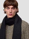 Man wearing a dark scarf and patterned sweater against a plain background