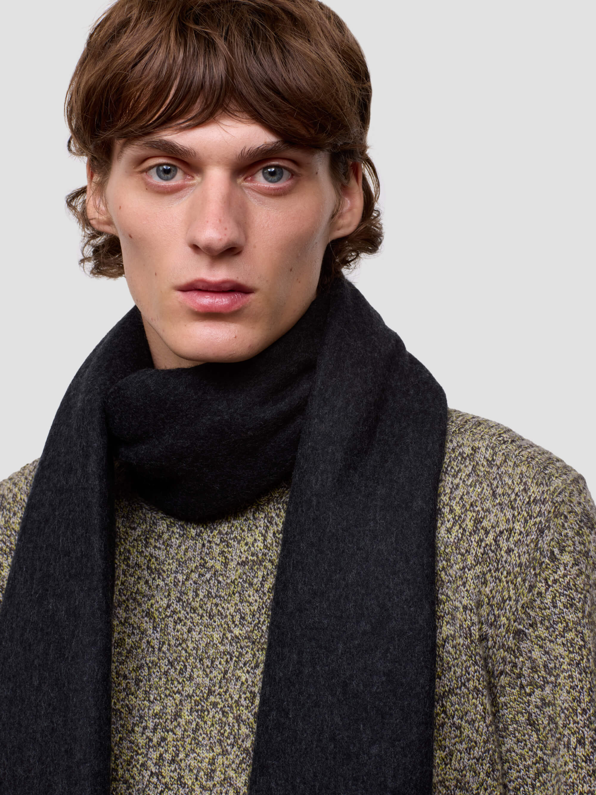 Man wearing a dark scarf and patterned sweater against a plain background